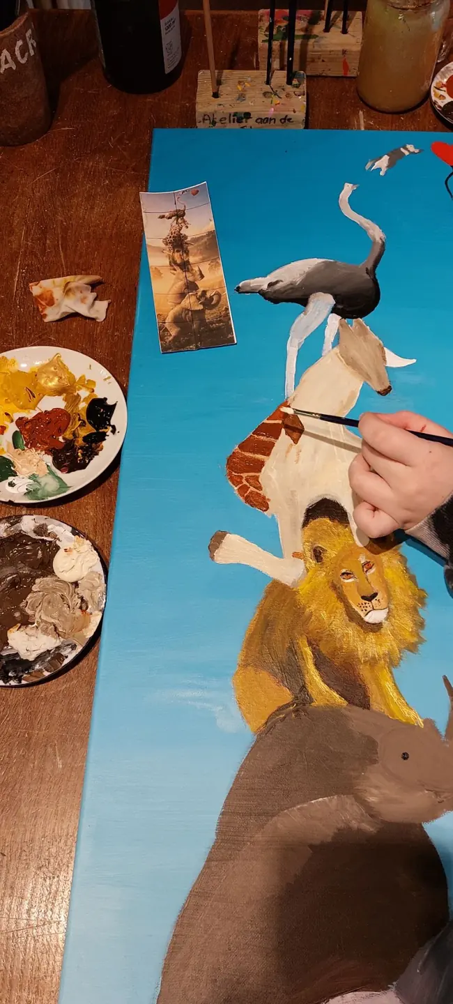 Een lang schilderij met dieren, met penselen en verf ernaast
