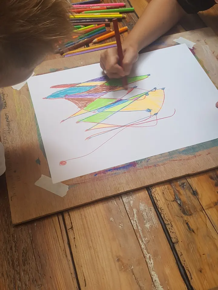 Een kind tekent met kleurpotloden op een groot vel papier