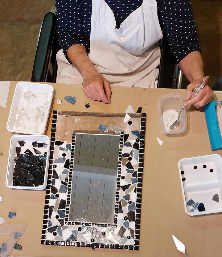 Iemand in een rolstoel werkt aan een mozaïekspiegel