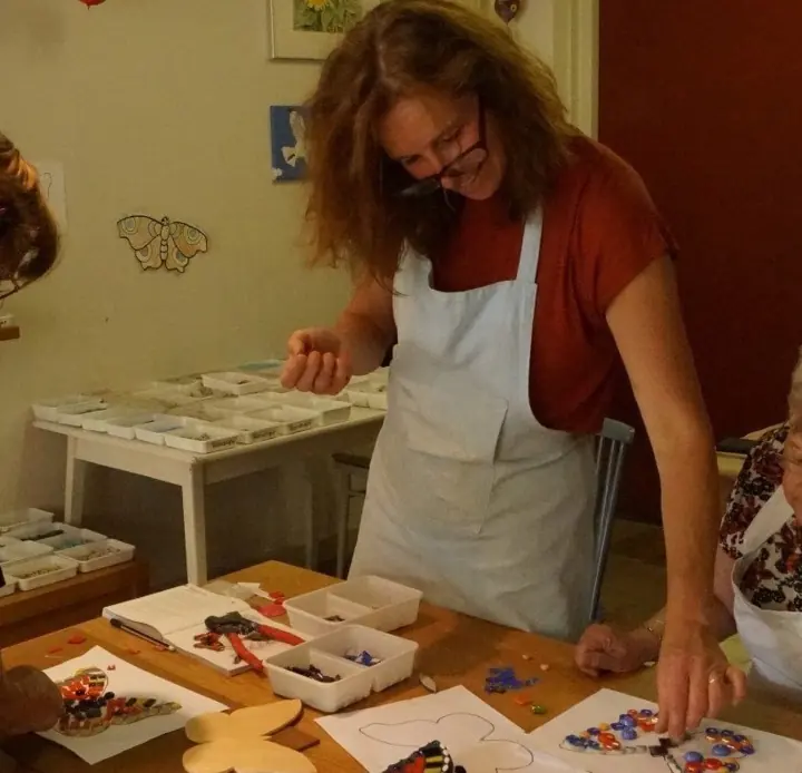 Ingrid aan de werktafel in het atelier, met bakjes mozaïeksteentjes